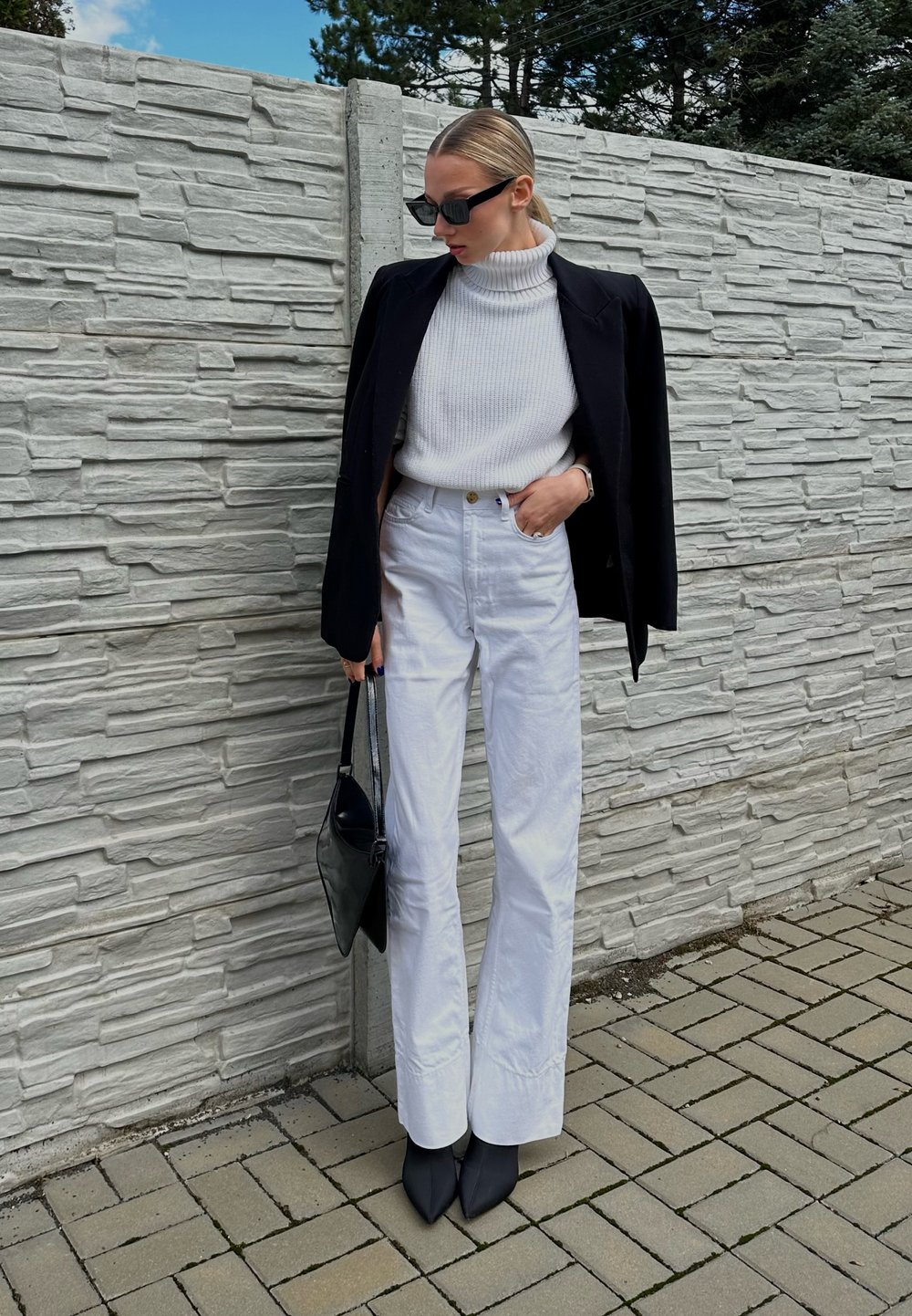 Calças largas brancas combinadas com um pulôver branco texturizado e um blazer preto. Os acessórios incluem uma mala preta e sapatos de salto pretos pontiagudos.