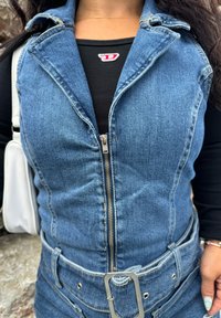 Τζιν φόρεμα με εφαρμοστή σχεδίαση, κλείσιμο με φερμουάρ και ζώνη στη μέση. Μπλε χρώμα με απαλό υφή, φοριέται πάνω από μια μαύρ�η μπλούζα.