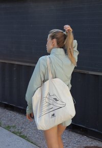 Lyseblå oversized jakke, beige tote bag med et skovide, og en hestehale frisure. Tekstureret stof og afslappet silhuet.