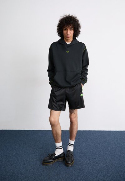 Sudadera negra con detalles verdes, pantalones cortos negros a juego y zapatos negros. Calcetines blancos con rayas negras y rojas. Diseño minimalista.