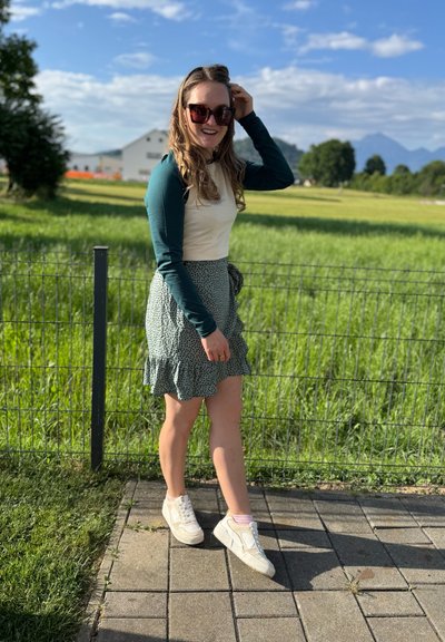 Una blusa verde de manga larga combinada con una falda verde clara con un patrón de lunares y un dobladillo con volantes. Zapatillas blancas con calcetas rosas.