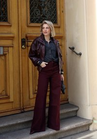 Burgundy wide-leg pants paired with a dark leather jacket over a gray shirt. The outfit features a textured finish and sleek black footwear.