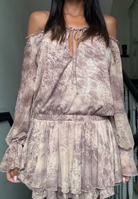 Blusa leve e estampada com design off-the-shoulder, featuring um decote ajustável com cordão, mangas longas e uma barra franzida e fluida.