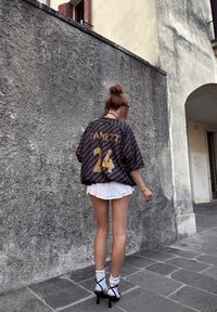 Jersey oversized às riscas pretas e cinzas com "ZANETTI" e o número "24" em dourado. Usado sobre uma saia branca, combinado com meias brancas e sapatos de salto.