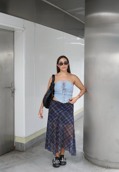 Top de corsé de mezclilla con parte delantera con cordones, falda envolvente de cuadros, bolsa negra y zuecos con adornos. Texturas suaves y material en capas.