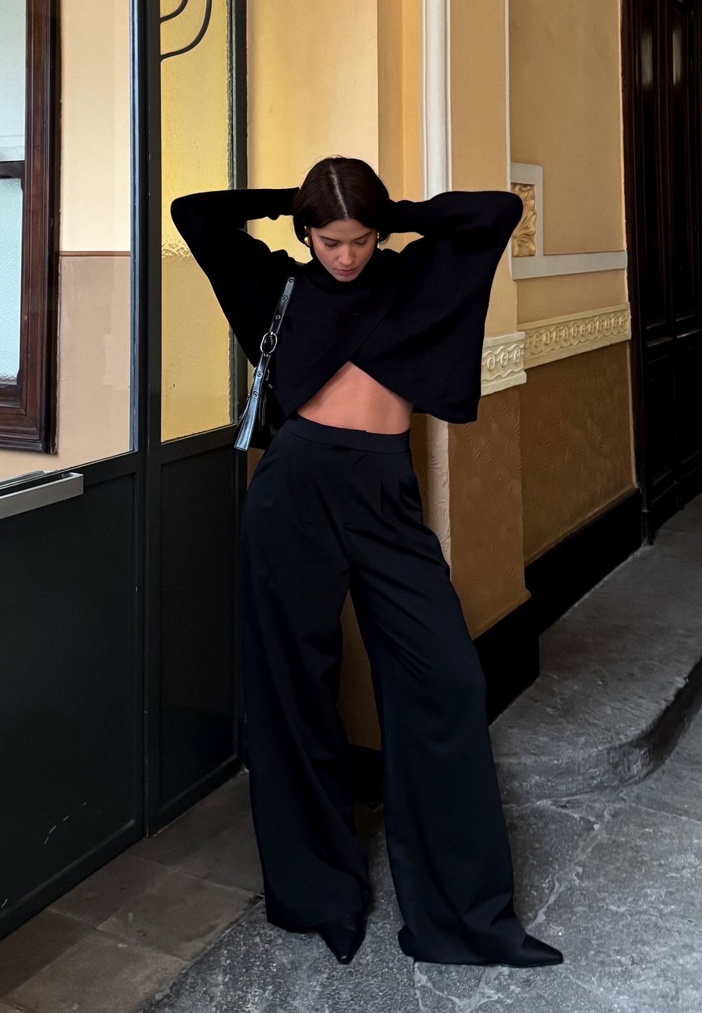 Suéter negro corto con una silueta amplia y un corte en la cintura, combinado con pantalones de pierna ancha de tiro alto en negro.