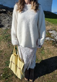 Suéter blanco de felpa, falda de encaje, bolso de mano amarillo con texto, botas marrones. Materiales texturizados; diseño suave, ligero y en capas.