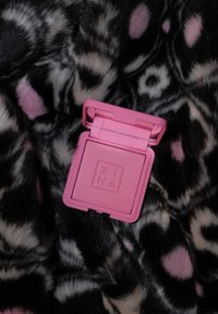 Rosa kompakt sminketui med preget "3INA"-logo, ligger åpent på en bakgrunn av svart og rosa mønstret pels.