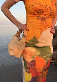 Borsa a spalla color beige con forma morbida e tessuto texturizzato, dotata di una tracolla robusta e accessori in argento, abbinata a un vestito floreale dai colori vivaci.