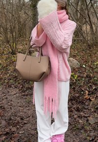 Pull en tricot rose pâle surdimensionné avec motif torsadé, associé à une longue écharpe rose. Sac fourre-tout en cuir marron à texture douce. Pantalon blanc.