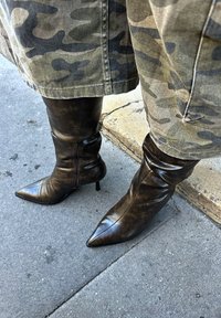 Brūnas ādas augstie zābaki ar norādītu purngalu un stiletto papēdi. Virsma ir ar faktūru, sānos ir rāvējslēdzējs aizdares nodrošināšanai.