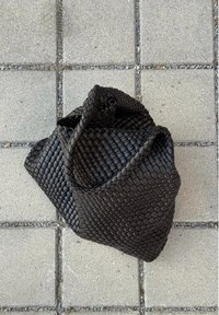 Borsa nera intrecciata realizzata in materiale testurizzato, caratterizzata da una forma unica con una parte superiore arrotondata e un design morbido e drappeggiato.