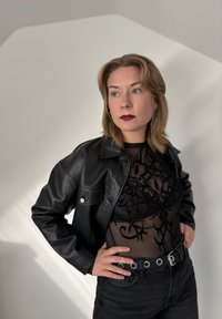 Must musta lõhikaga must nahktagi, mille all on läbipaistvast mustast materjalist lillemustriga topp, koos kõrge puusaga mustade teksade ja nõelatega vööd.  