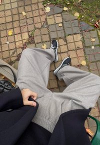 Grå, teksturerte joggebukser med elastisk liv, parret med svarte sportsko med hvite såler, som hviler på en mønstret brostein.