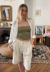 White button-up shirt over an olive green strapless top, paired with cream pleated shorts. Accessories include a bag and simple earrings.
