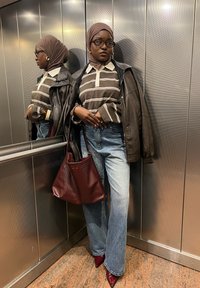 Brun og hvid stribet poloshirt under en sort læderjakke. Lys blå flagrende jeans, røde spidse hæle og en mørkerød strikket totebag.