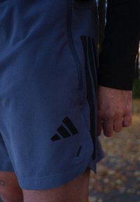 Jasnoniebieskie spodenki sportowe z czarnymi akcentami, z trójpasmowym wzorem. Wykonane z miękkiego materiału o fakturowanej powierzchni.