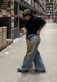 Jean à jambe large bleu clair avec une finition délavée et usée. Associé à un t-shirt noir et une chemise à manches longues rayée. Casquette camouflée.