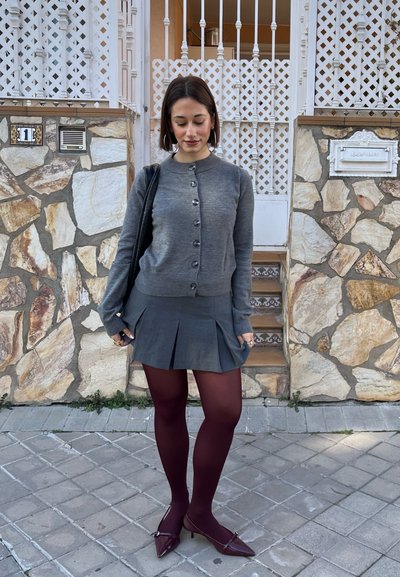 Cárdigan gris con botones, falda gris plisada, medias burdeos y tacones puntiagudos burdeos. Textura suave, diseño casual.