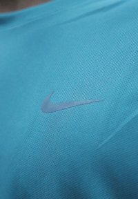 T-shirt de sport Nike en bleu clair, présentant une texture subtile et légèrement en relief avec un petit logo argenté sur le côté gauche de la poitrine.