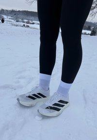 Άτομο που φοράει μαύρο κολάν και λευκά αθλητικά με μαύρες ρίγες, στέκεται σε χιονισμένο έδαφος σε εξωτερικό χώρο.