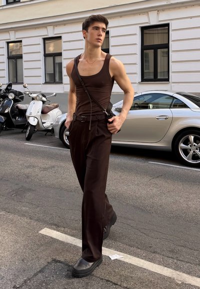 Top sin mangas marrón combinado con pantalones marrones holgados, acentuado por un bolso de hombro y zapatos negros gruesos, todo ello en una calle de la ciudad.