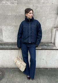 Tumši zila džinsa pūkaina jaka kopā ar izplešamām džinsa biksēm. Aksesuāri: melnas cimdi un bēša soma. Vienkāršas faktūras un līnijas.