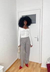 Top de manga longa branco em tecido com nervuras e design off-shoulder, calças de cintura alta em xadrez cinza, sapatos vermelhos de bico fino e uma pequena bolsa de creme.