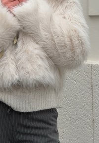 Ψεύτικο γούνινo μπουφάν σε κρέμα χρώμα με αφράτη υφή, διαθέτει πλέκτο μπεζ τελείωμα. Συνδυασμένο με σκούρες ρίγες παντελόνι, δημιουργώντας μια πολυάριθμη εμφάνιση.