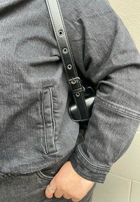 Γκρι τζάκετ από τζιν με πλευρική τσέπη και ορατές ραφές. Μια μαύρη δερμάτινη ταινία με μεταλλικά στοιχεία είναι προσαρτημένη στο τζάκετ.