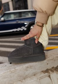 Stivale alla caviglia in suede grigio con suola in gomma piatta. Presenta dettagli di cucitura, un pratico tassello posteriore e una tomaia testurizzata. Indossato con pantaloni chiari.