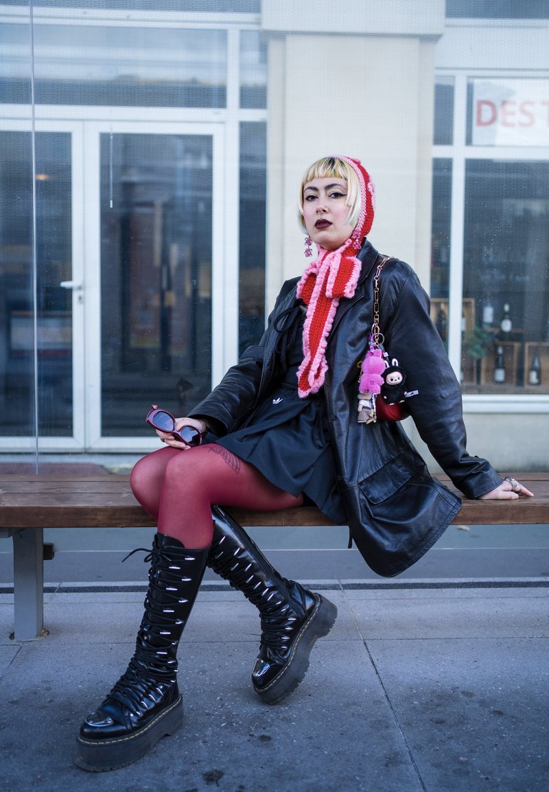 Black leather oversized jacket, pink scarf, red tights, and black high-heeled lace-up boots. Accessories include pink and black plush charms.