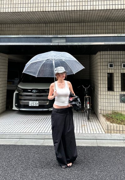 Sombrilla clara y transparente con una tapa plateada, combinada con una camiseta blanca y pantalones anchos negros, de pie en un área exterior de cerámica.