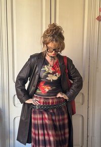 Καφέ δερμάτινο παλτό πάνω από ένα τοπ με λουλουδάτο σχέδιο, καρό φούστα με διακοσμητική μαύρη ζώνη και κόκκινη τσάντα ώμου. Σκοτεινά γυαλιά ηλίου και κοσμήματα.