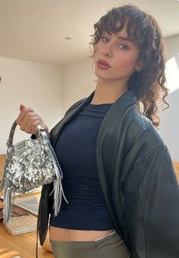 Sac en sequins argentés avec une forme arrondie et une courte anse, associé à un haut ajusté bleu marine et une veste en cuir noire.