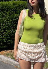 Zöld ujjatlan body, gyűrt részletekkel, amelyet egy zöldet mini szoknyával párosítanak, világos rózsaszín rétegezett mini szoknya, kerek flitterekkel és fehér derékrésszel.