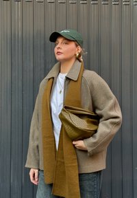 Barna gyapjúkabát szürke béléssel, barna kötött sállal és zöld táskával párosítva. A modellen zöld sapka és fehér ing található.
