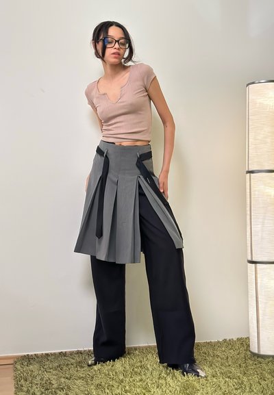 Falda gris con plisados y acentos negros, combinada con una blusa de punto ribeteada en beige claro. El conjunto incluye pantalones negros de pierna ancha y zapatos elegantes.