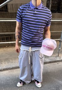 Fialovo-čierny pruhovaný polo tričko, šedé teplákové nohavice s vreckami, ružová a šedá čiapka s textom "VON DUTCH", ružové tenisky.