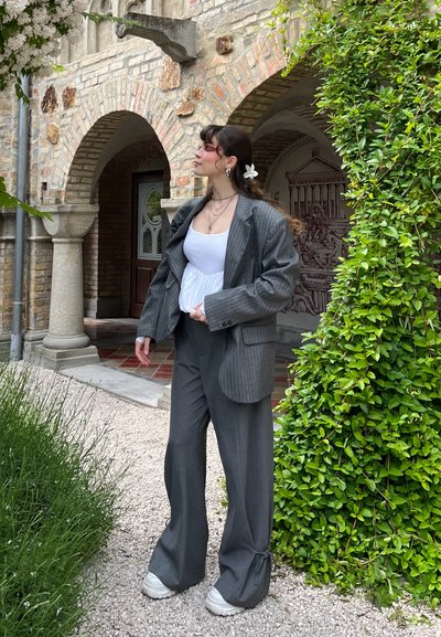 Blazer oversize gris de rayas, combinado con pantalones grises sueltos, acentuado por una blusa blanca y zapatillas gruesas, todo esto sobre un fondo de vegetación.