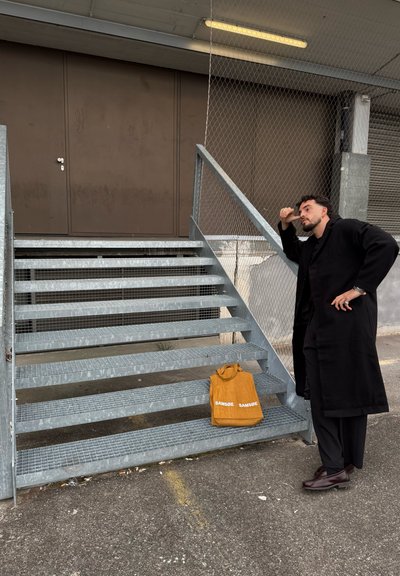 Escaleras exteriores de color gris metálico con laterales de malla, que conducen a una puerta marrón. Una bolsa de color mostaza colocada en el peldaño inferior, que exhibe "SAMSOE."