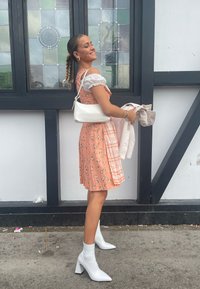 Kleid mit floralen Mustern in Pfirsichfarbe, mit weißen, gerafften Ärmeln; kombiniert mit einer weißen Tasche im Krokodilmuster und weißen Knöchelschuhen.