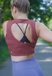 Bordeaux sportieve crop top met een uitgesneden achterkant, gecombineerd met een zwarte sport-bh eronder. Bevat subtiele perforaties en een aansluitend ontwerp.