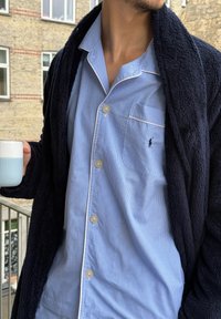 Mornarsko mehak kako nad svetlo modro karo srajco z belim obrobe in žepom na prsih, drži svetlo modro teksturirano skodelico.