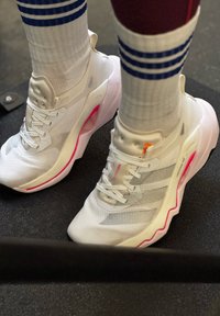 White trainers with mesh fabric and pink accents. Features include a textured sole, lacing system, and visible branding.