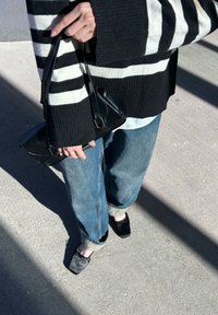 Μαύρο και λευκό ριγέ υπερμεγέθη πουλόβερ, ανοιχτό μπλε πουκάμισο, φαρδιά τζιν παντελόνια και μαύρη τσάντα. Μαύρα σανδά�λια με τετράγωνη μύτη.