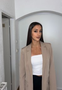 Béžový blazer s klopami, zapínaním na jeden gombík a dvoma prednými vreckami, nosený cez biely crop top a čierne nohavice. Hladká štruktúra.