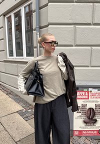 Beige top met lange mouwen met patroon op de mouwen, zwarte handtas, donkere wijde broekspijpen en een bruine leren jas. Grote zonnebril maakt de look compleet.