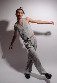 Gilet à rayures grises et pantalon assorti, fabriqués en tissu léger. Chaussures noires à semelles épaisses. Le modèle pose avec un bras tendu contre un fond uni.