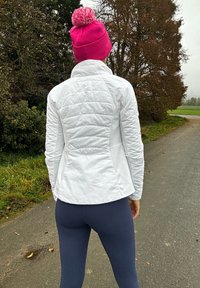 Bijela prešana jakna sa strukturiranim dizajnom, u kombinaciji s tamnoplave hulahopke. Svijetloružičasta pletena kapa s pom-pom naglaskom upotpunjuje outfit.